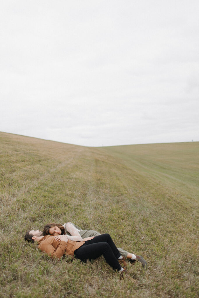 A couple laying in a huge grass field during their engagement photos at Holmes Lake in Lincoln, Nebraska. 