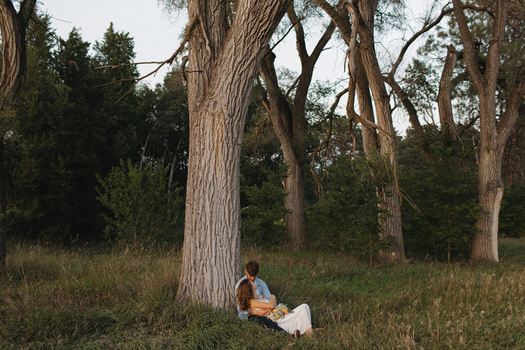 Couple poses for engagement pictures  under large tree at Pioneers Park in Lincoln, Nebraska.