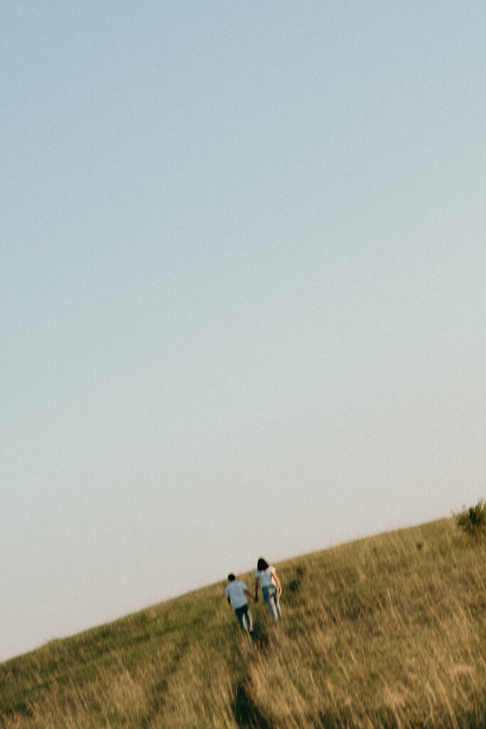 A couple running through a field during their engagement photo session at Spring Creek Prairie Arboretum in Nebraska. 