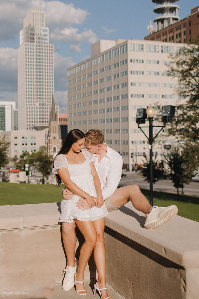 A couple taking engagement photos outside of Central High School with Downtown Omaha Nebraska in the background 