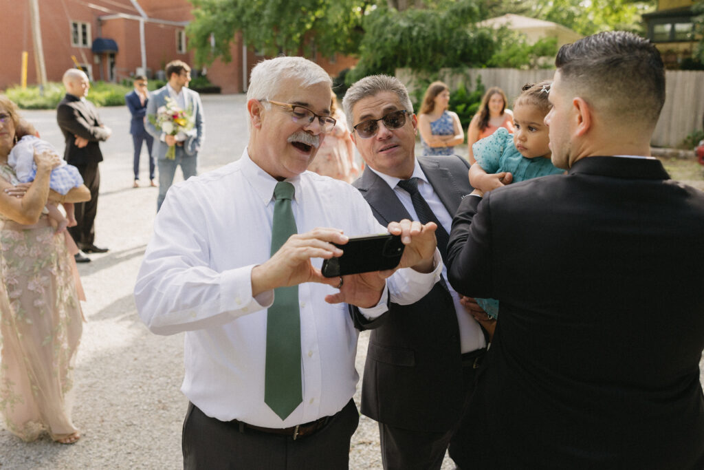 Documentary wedding photographer captures father of the bride sharing photos on his phone