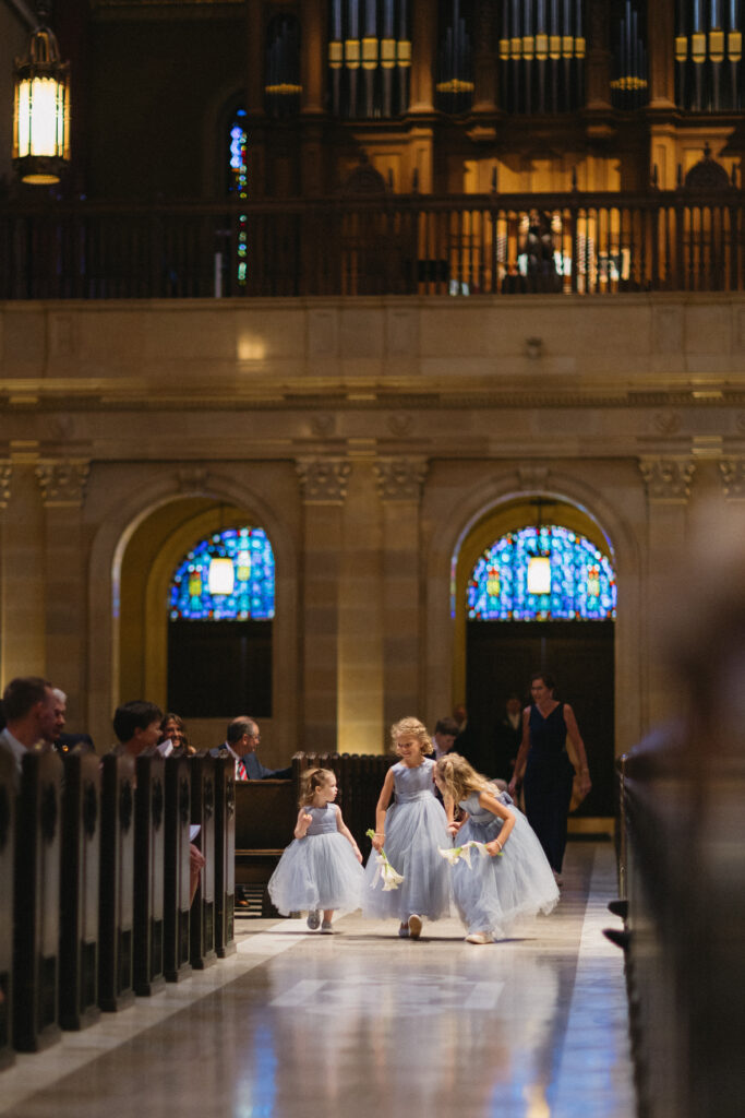 flower girls walk down long cathedral aisle before catholic 