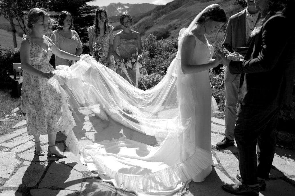 bridesmaid adjusts the bride's train as she stands at the alter. 