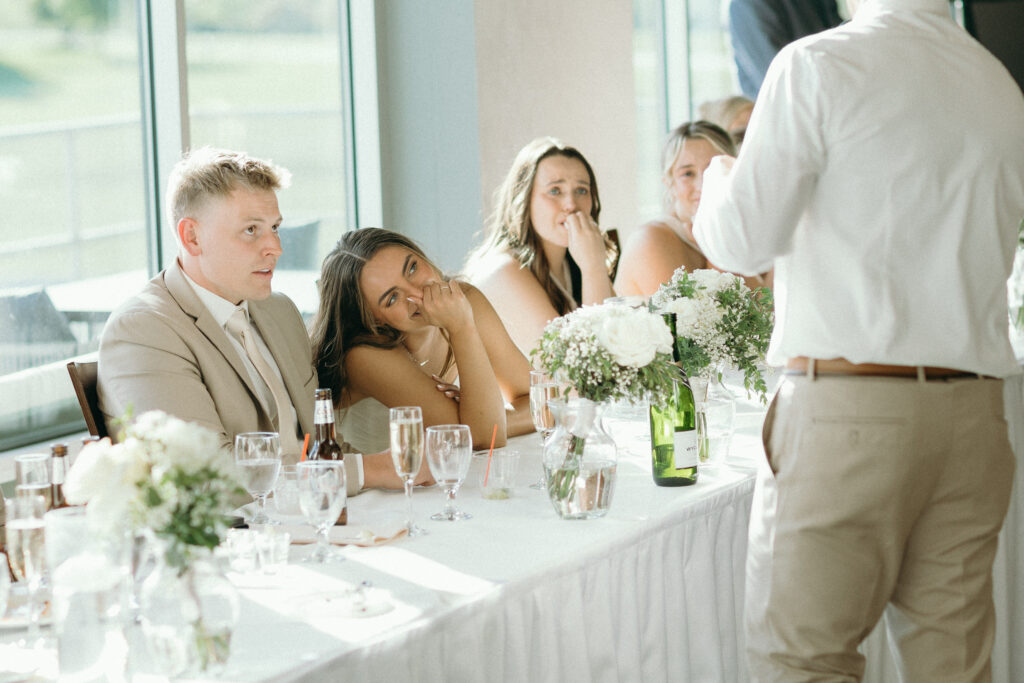 bride and groom listen as the best man gives his speech at their wedding reception 