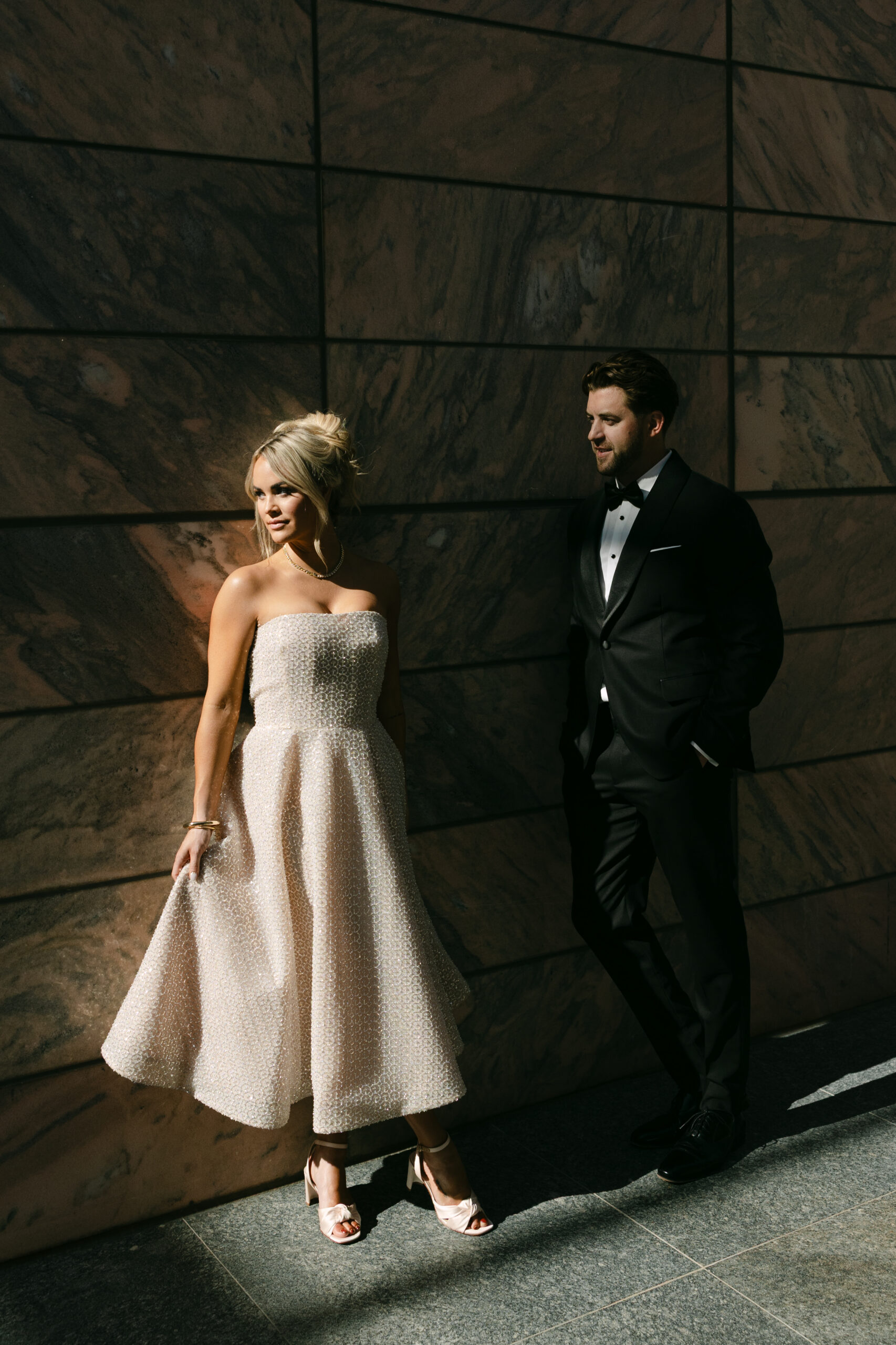 engaged couple standing in front of wall in evening light