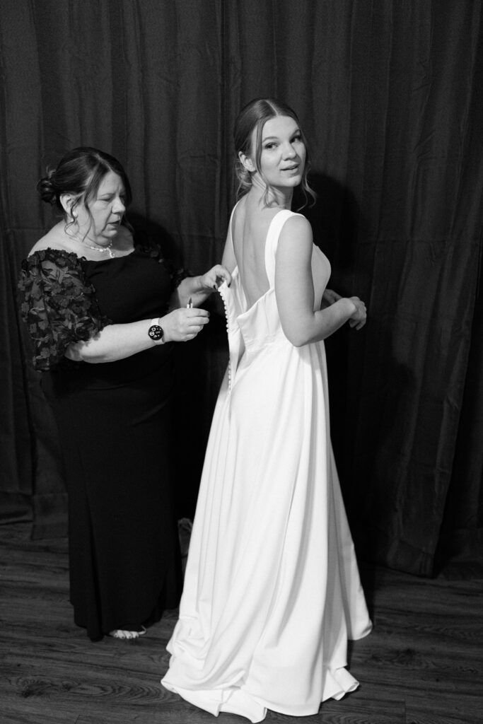 mother helps bride into wedding dress